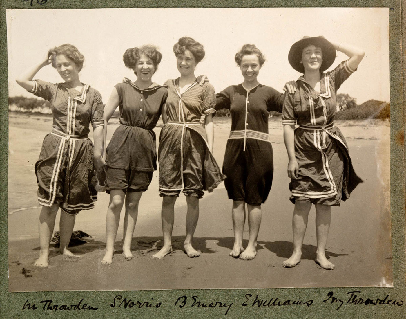 Sepia photo of five women on the beach wearing woolen one suit style swimmers down to the knee.